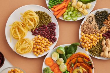 A vibrant mix of legumes, vegetables, nuts, and pasta arranged on white plates showcasing a balanced, healthy diet.